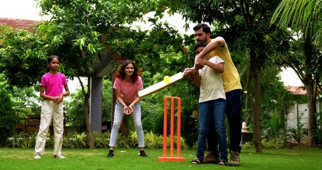 Indian family playing cricket batting in home garden, spending quality fun time together playing outdoor sports, cheerful Asian parents and children enjoying backyard activity bonding on sunny day