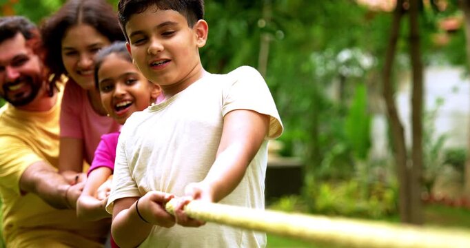 Indian family playing tug of war rassi khech in home garden, spending quality fun time together enjoying outdoor sports, cheerful Asian parents children bonding through traditional backyard activity