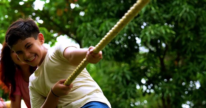 Indian family playing tug of war rassi khech in home garden, spending quality fun time together enjoying outdoor sports, cheerful Asian parents children bonding through traditional backyard activity