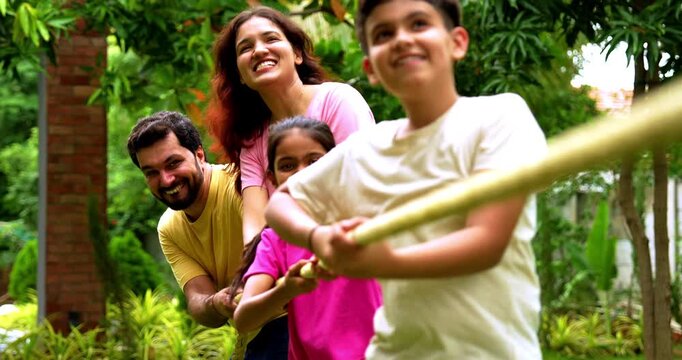 Indian family playing tug of war rassi khech in home garden, spending quality fun time together enjoying outdoor sports, cheerful Asian parents children bonding through traditional backyard activity