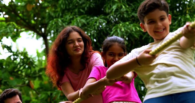 Indian family playing tug of war rassi khech in home garden, spending quality fun time together enjoying outdoor sports, cheerful Asian parents children bonding through traditional backyard activity