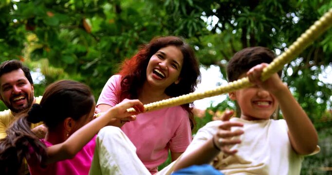 Indian family playing tug of war rassi khech in home garden, spending quality fun time together enjoying outdoor sports, cheerful Asian parents children bonding through traditional backyard activity