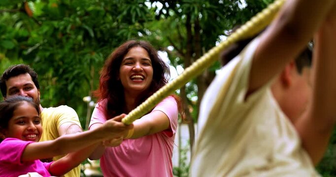 Indian family playing tug of war rassi khech in home garden, spending quality fun time together enjoying outdoor sports, cheerful Asian parents children bonding through traditional backyard activity