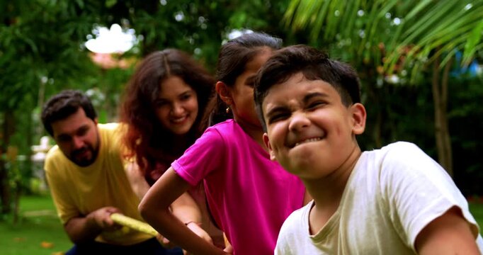 Indian family playing tug of war rassi khech in home garden, spending quality fun time together enjoying outdoor sports, cheerful Asian parents children bonding through traditional backyard activity