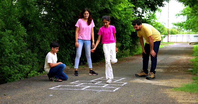 Indian family playing Tikkar Billa, a traditional hopscotch game in home garden, spending quality fun time together with children hopping on squares and enjoying nostalgic outdoor sports activity