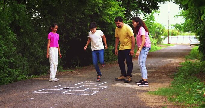 Indian family playing Tikkar Billa, a traditional hopscotch game in home garden, spending quality fun time together with children hopping on squares and enjoying nostalgic outdoor sports activity
