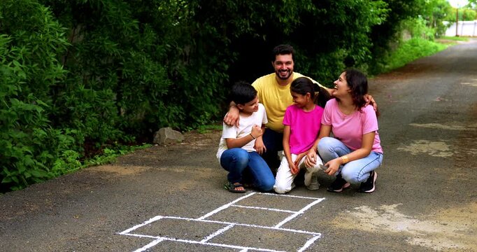 Indian family playing Tikkar Billa, a traditional hopscotch game in home garden, spending quality fun time together with children hopping on squares and enjoying nostalgic outdoor sports activity
