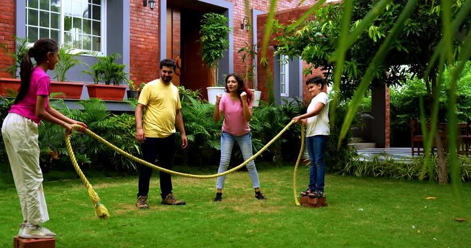 Indian kids playing tug of war or rassi khech in home garden while parents cheer them, spending quality fun time together enjoying traditional outdoor sports bonding during weekend family activity