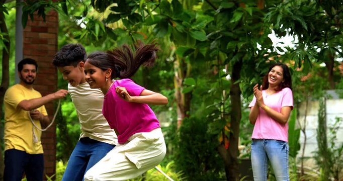 Indian family playing jumping rope in home garden, spending quality fun time together enjoying outdoor sports, cheerful Asian parents children bonding through traditional fitness activity in backyard