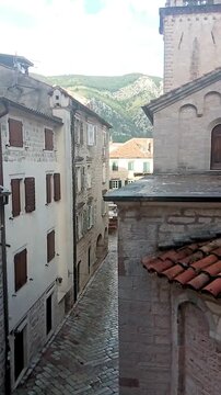 View of historic stone buildings with red tiled roofs, narrow street and the rear facade of Saint Tryphon Cathedral in the old town of Kotor. Balkan heritage and medieval architecture in Montenegro