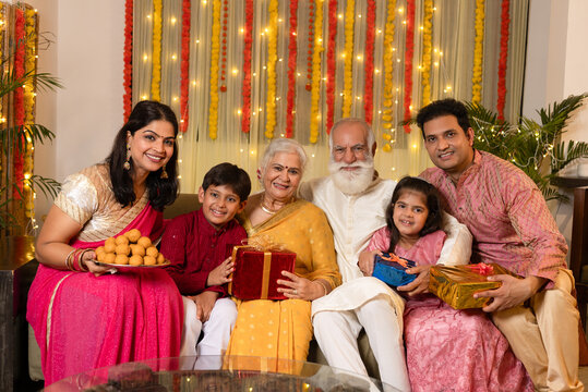 Indian happy joint family celebrating Diwali festival with full thali of laddu and gifts on the occasion of Diwali season in colorful decorated home background - Diwali holidays festive