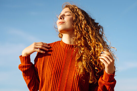 Portrait of young woman in casual clothes enjoying sunny day on sandy beach. Cute woman smiling, having fun and enjoying sunset outdoors. Leisure and nature concept.