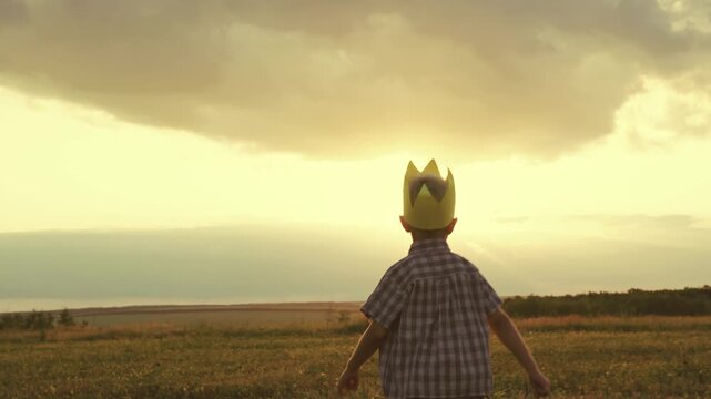 little child boy runs across field with crown head. superhero sun glare light. happy childhood active playful kid. child runs merrily sunset. free adventure kid game. son childhood dream. farming.
