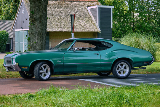 Classic Green Oldsmobile Cutlass Muscle Car parked in rural road with rural background