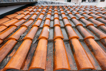 Rainwater flows down orange roof tiles: roofing and gutter system maintenance