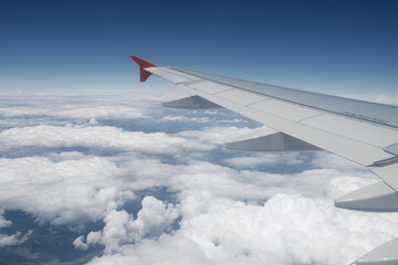 Obraz premium A peaceful in-flight view from a passenger seat showing an aircraft wing soaring above soft clouds under a bright blue sky.