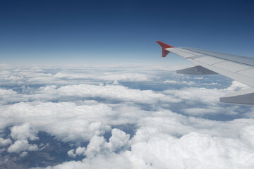 Fototapeta premium A peaceful in-flight view from a passenger seat showing an aircraft wing soaring above soft clouds under a bright blue sky.