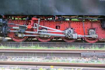 detailed close-up of steam locomotive undercarriage showing red wheels, connecting rods, pistons and steel mechanics – precision engineering from the age of steam power