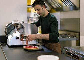 Chef slicing meat with professional electric slicer in restaurant kitchen