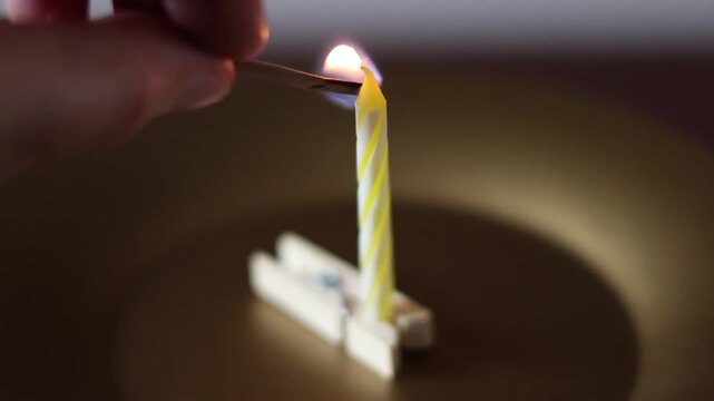 Una toma de cerca de una vela blanca con amarillo de cumplea&ntilde;os  con llama colocada en un gancho de madera en un fondo oscuro  
