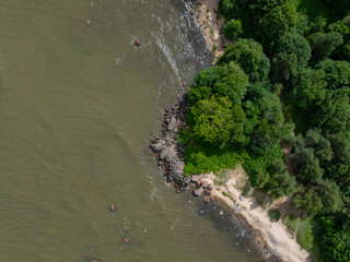 Top down photo of a transitional zone where sandy beach meets rocky terrain. In the center, a cluster of larger, moss-covered rocks extends into the water. Sandy Türisalu beach on the right side. 