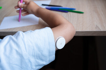 Child drawing with continuous glucose monitoring system on arm
