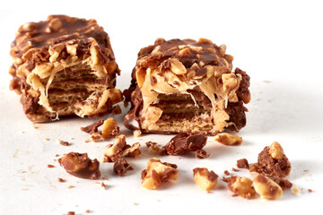 two broken chocolate wafer caramel bars sprinkled with peanuts isolated on white background.