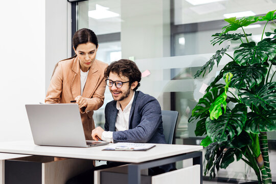 A business man and woman brainstorm over a laptop in a modern office. Concept collaborative decision-making and innovative ideas.