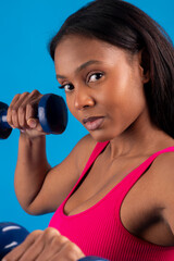 Fototapeta premium Determined black model lifting weights on blue background