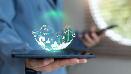 Close-up hand holding tablet with hologram of wind energy, CO2 reduction, and smart eco-home icons, representing green innovation and clean energy technology in business.