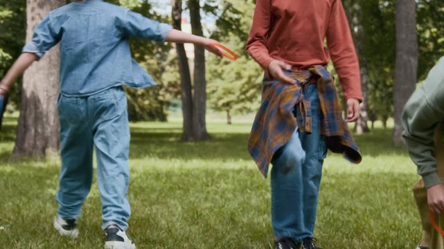 Tilt down shot of three children gathering up colourful rings after unsuccessful try to toss them around pegs in park