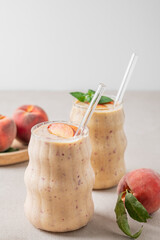 Two glasses of smoothie with peach and banana on a light background with tropical fruits.
