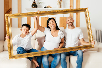 Eurasian Family Joyfully Posing With a Large Frame in a Cozy Indoor Setting