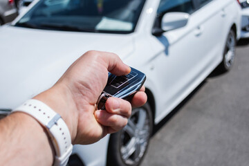 Man holds a car key in a parking lot with several cars. The concept of remote car opening and vehicle rental in dealership. © vadish
