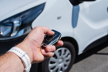 Obraz premium Man holds a car key in a parking lot with several cars. The concept of remote car opening and vehicle rental in dealership.