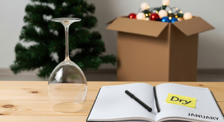 Dry January Challenge. Empty wine glass turned upside down on table after New Year celebration. Back to normal reality, self reflection journal diary and pen