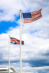 UK and US flags waving side by side on flagpoles against a cloudy sky, symbolizing international relations and historic ties