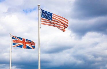 UK and US flags waving side by side on flagpoles against a cloudy sky, symbolizing international relations and historic ties
