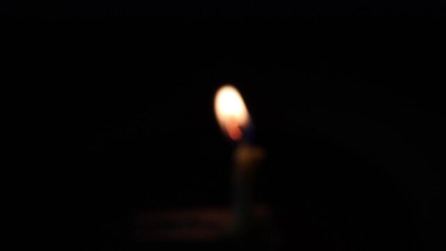 Una toma de cerca de una vela blanca con amarillo de cumplea&ntilde;os  con llama desenfocada colocada en un gancho de madera en un fondo oscuro  