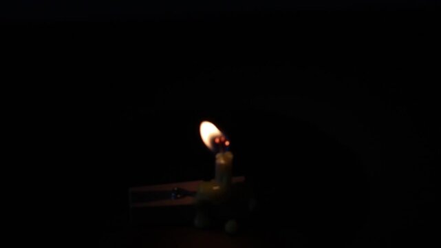 Una toma de cerca de una vela blanca con amarillo de cumplea&ntilde;os  con llama desenfocada colocada en un gancho de madera en un fondo oscuro  