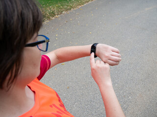 Woman wearing glasses and a blue t-shirt, standing outdoors in a park. He is looking down and...
