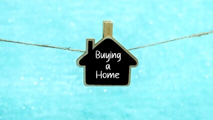 BUYING A HOME symbol. BUYING A HOME written on a mini blackboard in the shape of a house. light blue background.