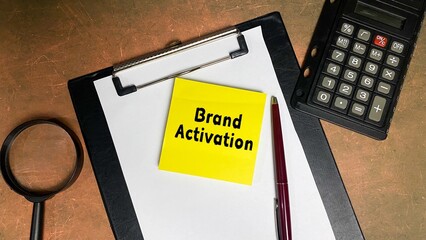 BRAND ACTIVATION written on a sticky note isolated on a work desk. Calculator and pen as decoration.