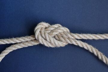 Fototapeta premium Thick rope knot on blue background. Hemp rope with knot.