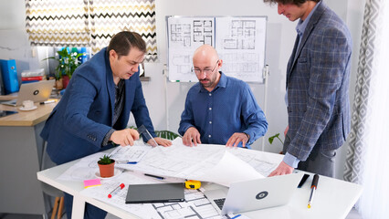 A man with a triangle ruler points to the drawings and asks the architect for the construction time...