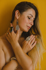 Portrait of a girl with long hair on the background of a yellow wall in costume jewelry