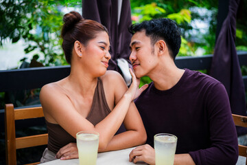 Flirty girlfriend gently stops her eager boyfriend from kissing her during a date at an alfresco cafe.
