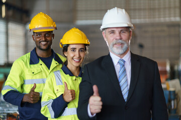 A foreman and worker are standing in a factory, looking standing pose. They wear a yellow and white safety helmet for safety.