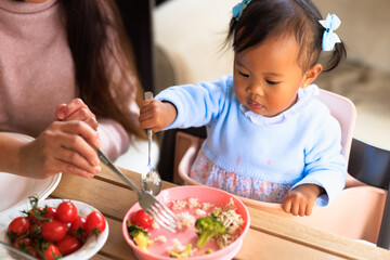 HIgh view of toddler girl holding cutlery at lunch being helped by her mother