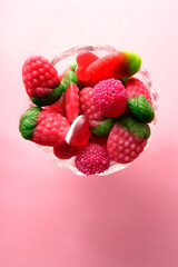 Bowl overflowing with colorful, sugary gummy candy on pink background